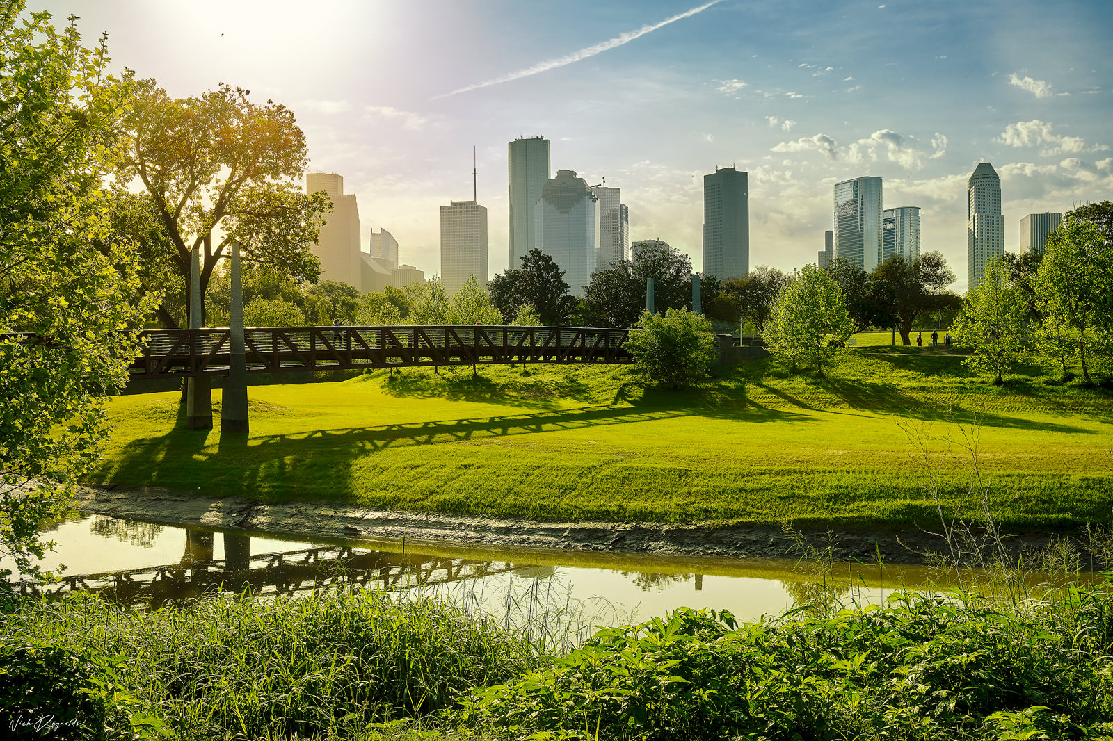 Buffalo Bayou Park and trail with a view of the bayou, pedestrian bridge, and downtown Houston